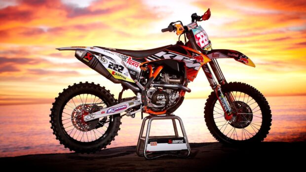 A KTM dirt bike displayed against a vibrant sunset over the ocean