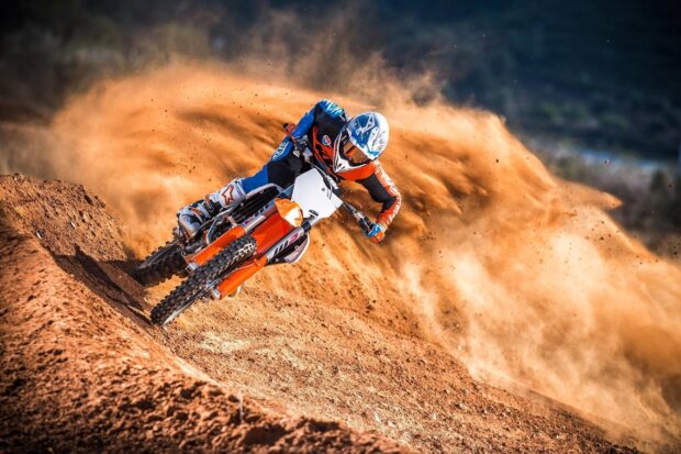 A KTM dirt bike rider kicks up dirt while making a sharp turn on a motocross track