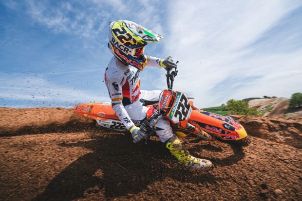 A KTM dirt bike rider wearing full gear powers through a dirt track on a bright day
