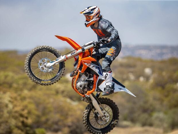 A rider performing a stunt on an orange KTM dirt bike in an outdoor desert setting