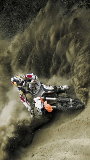 A rider on an orange KTM dirt bike kicks up dust while racing on a sandy track