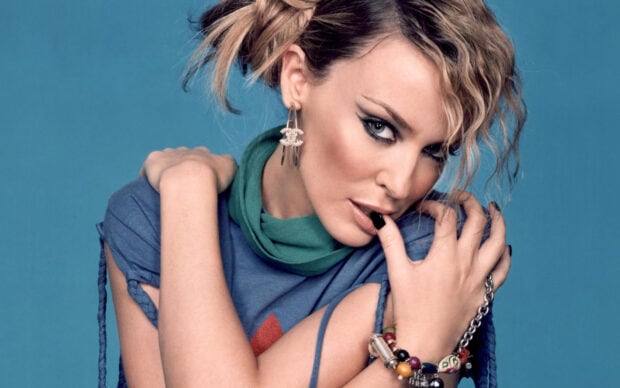 Kylie Minogue is posing with a hand near her mouth and wearing colorful bracelets, HD Desktop Wallpaper