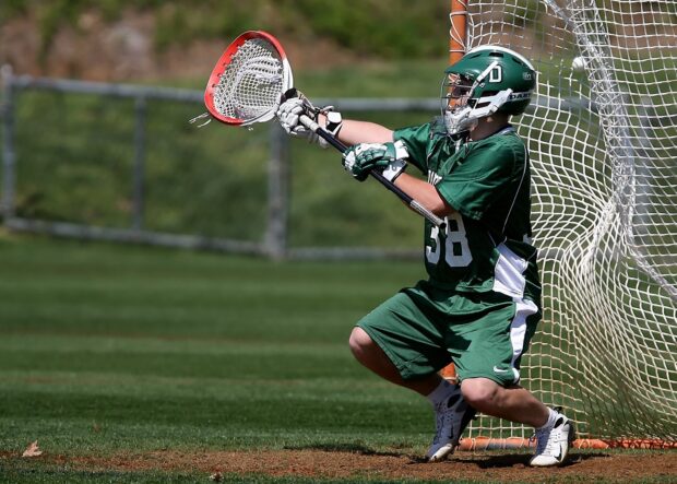 A lacrosse goalie in green uniform catching the ball near the net during a game, HD Desktop Wallpaper