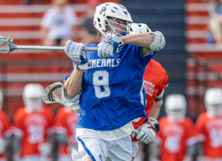 Lacrosse player in blue uniform with helmet and gloves during game on field.