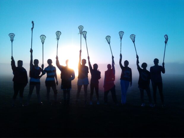 A group of lacrosse players stand silhouetted against the sunrise holding their lacrosse sticks raised in celebration, HD Desktop Wallpaper