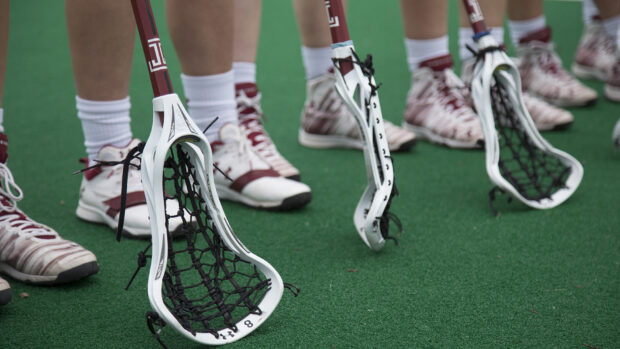 Lacrosse sticks held by players standing on green turf, HD Desktop Wallpaper