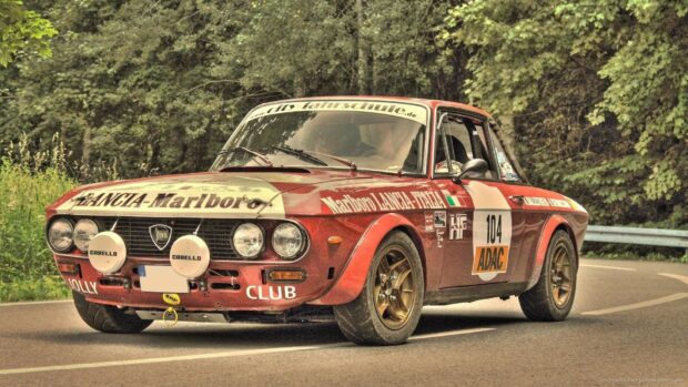 Vintage Lancia rally car driving on a forest road with racing decals, HD Desktop Wallpaper