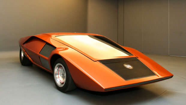 A bright orange Lancia with a futuristic sleek design is displayed indoors, 2K Desktop Wallpaper