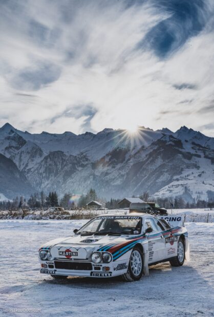 A Lancia racing car with Martini livery is parked on snow with mountains in the background, 2K Mobile Wallpaper