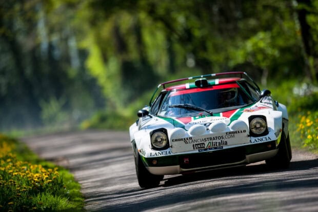 A Lancia vehicle races along a curvy forest road surrounded by greenery and flowers, HD Desktop Wallpaper