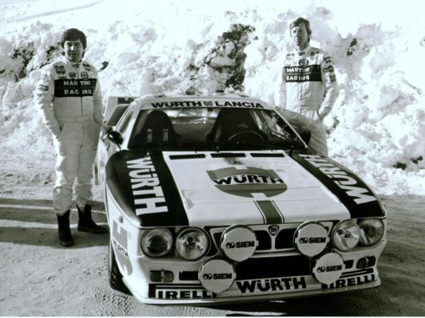 Two drivers stand beside a Lancia racing car in snowy conditions showing classic rally style, HD Desktop Wallpaper