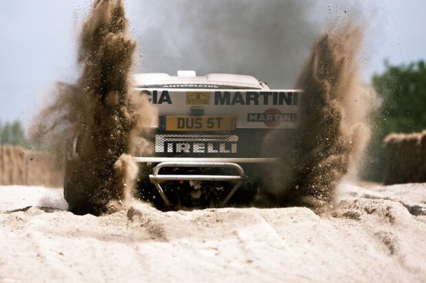 A Lancia Wallpapers rally car is driving through sand kicking up dust, HD Desktop Wallpaper