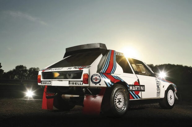 A Lancia rally car with Martini racing stripes is shown under the sunset sky, HD Desktop Wallpaper
