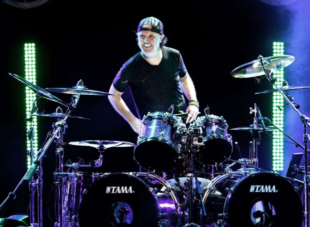 Lars Ulrich is smiling while playing drums during a live concert, 2K Desktop Wallpaper