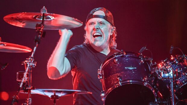 Lars Ulrich is playing drums with intense expression during a live concert, HD Desktop Wallpaper