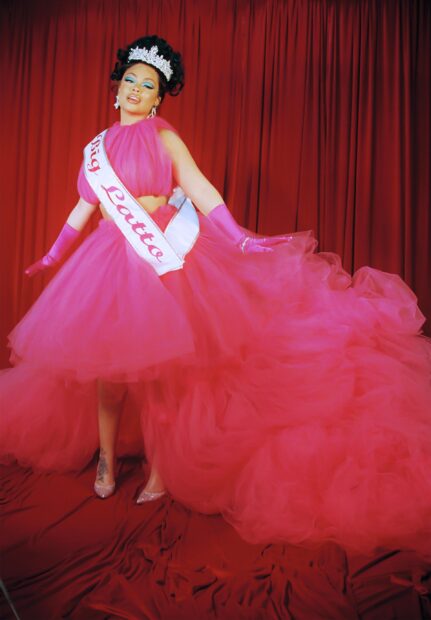 Latto wears a flowing pink gown with a tiara and sash in front of a red curtain, 2K Desktop Wallpaper