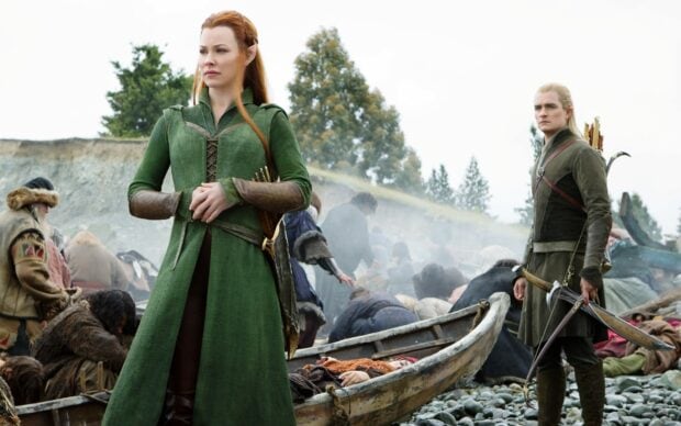 Legolas standing with a woman in green elven attire on a rocky shore after a battle