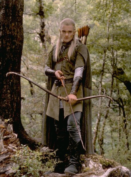 Legolas standing with a bow in the forest holding an arrow ready to shoot