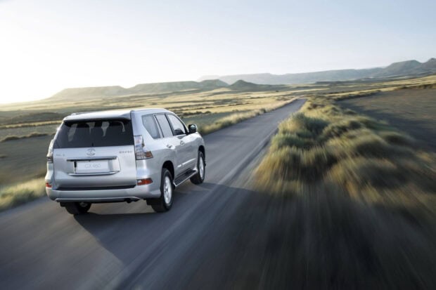 A Lexus GX drives along a remote road through a dry landscape with mountains in the distance, HD Desktop Wallpaper