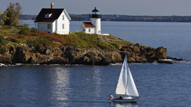 A sailboat sails near a lighthouse on a rocky coast in Maine in this scenic view of Maine wallpapers, HD Desktop Wallpaper