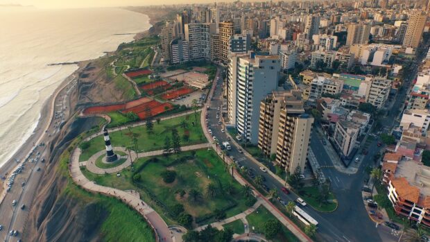 The Lima Peru Wallpapers show a coastal cityscape with buildings and a lighthouse under the setting sun, 4K Desktop Wallpaper