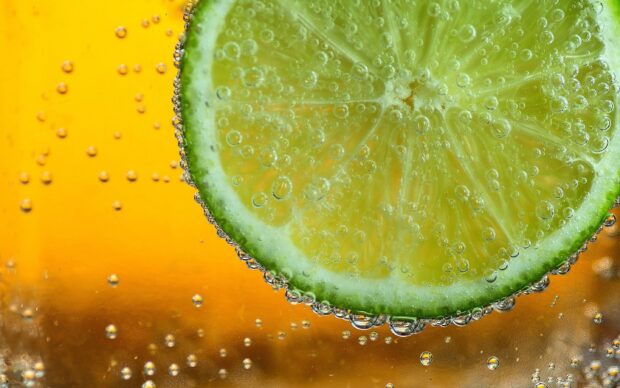 Close up of lime slice with bubbles in sparkling water on orange background