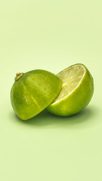 Fresh lime cut in half on a light green surface with a smooth texture