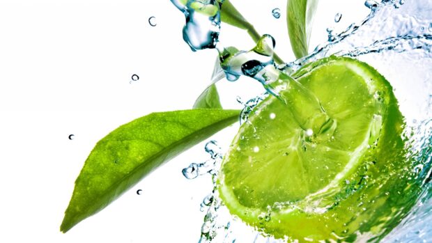 Fresh lime slice with green leaves splashing in clear water with bubbles