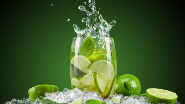 A refreshing glass of lime slices with mint and ice splashing in water