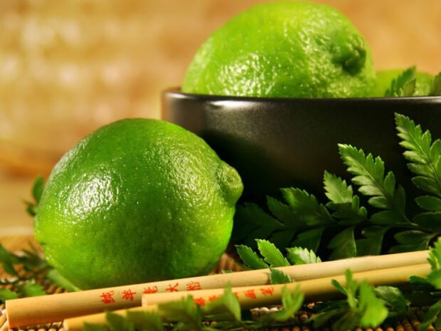 Fresh lime fruit with green leaves and chopsticks on a rustic surface