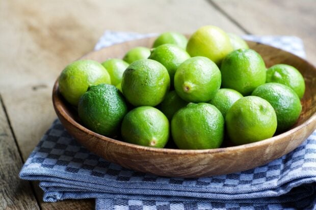 A bowl of fresh green lime on a wooden table with a checkered cloth