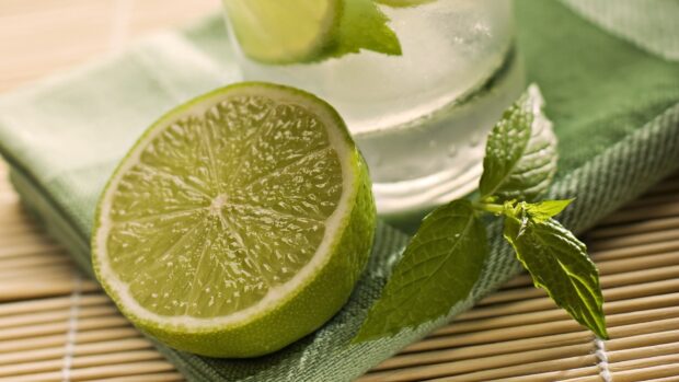 Fresh lime half with mint leaves on a green cloth near a glass of water