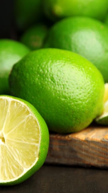 Close up of fresh lime on wooden surface with juicy lime slice in front