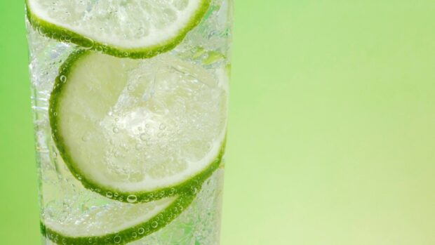 Fresh lime slices immersed in sparkling water with bubbles on a green background