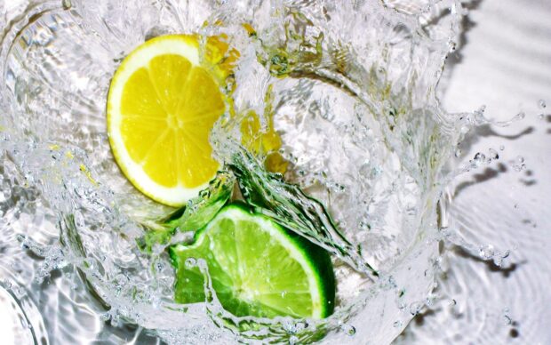 A fresh lime slice splashing into clear water with a lemon slice nearby
