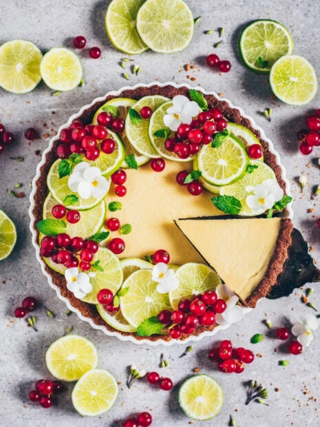 A tart decorated with fresh lime slices and red currants on a gray surface
