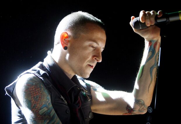 A tattooed musician from Linkin Park performing passionately on stage with a microphone in hand