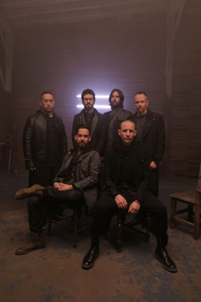 Linkin Park band members posing in a dimly lit room with a neon light in the background