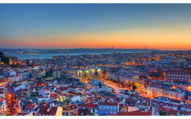 The cityscape of Lisbon Portugal is beautifully lit during sunset with the river and bridge in view, HD Desktop Wallpaper