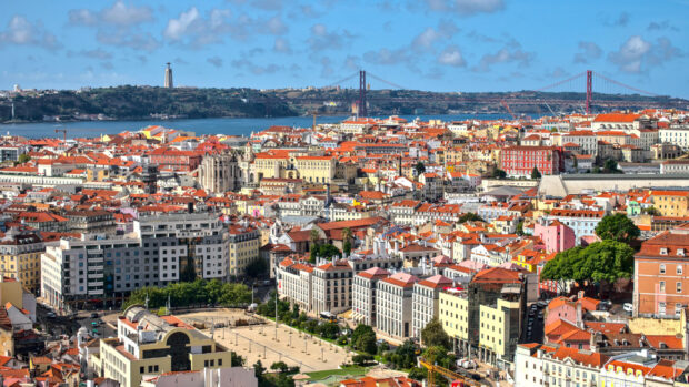 A vibrant cityscape of Lisbon Portugal with historic buildings and a bridge over the river, 2K Desktop Wallpaper