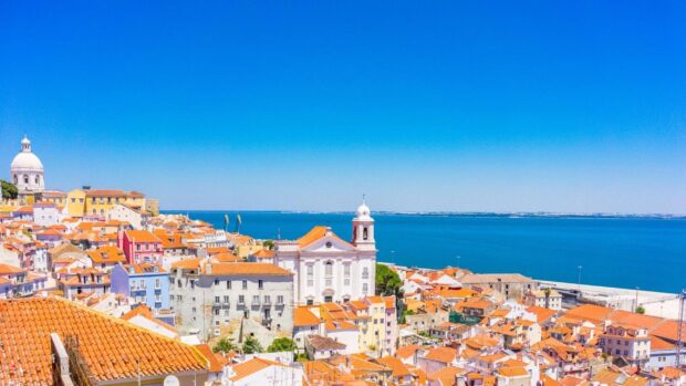 A scenic view of Lisbon Portugal with colorful buildings and ocean under a clear blue sky, 2K Desktop Wallpaper