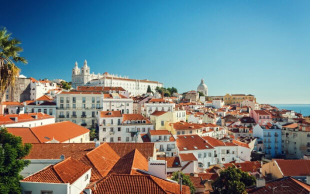 A scenic view of Lisbon Portugal cityscape featuring historic buildings and red rooftops under a clear blue sky