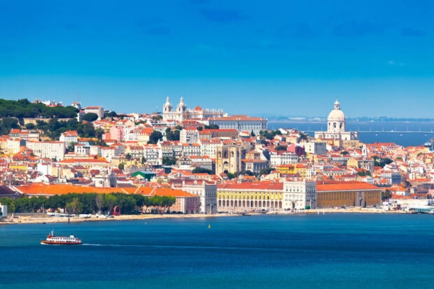 A vibrant Lisbon Portugal cityscape is seen with buildings and a boat on the river, HD Desktop Wallpaper