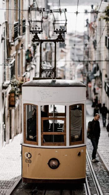 A yellow tram is traveling through a narrow street in Lisbon Portugal with people walking nearby, HD Mobile Wallpaper