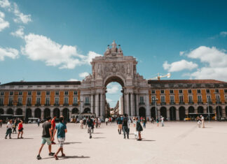 People walking near a historic arch in Lisbon Portugal during the day, 2K Desktop Wallpaper