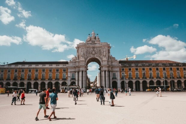 People walking near a historic arch in Lisbon Portugal during the day, 2K Desktop Wallpaper