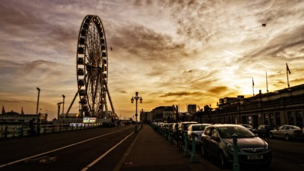 The London Eye stands tall at sunset over a busy city street with cars parked along the road, 4K Desktop Wallpaper