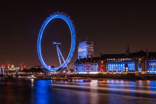 The London Eye glowing blue over the river Thames with illuminated buildings nearby, 2K Desktop Wallpaper