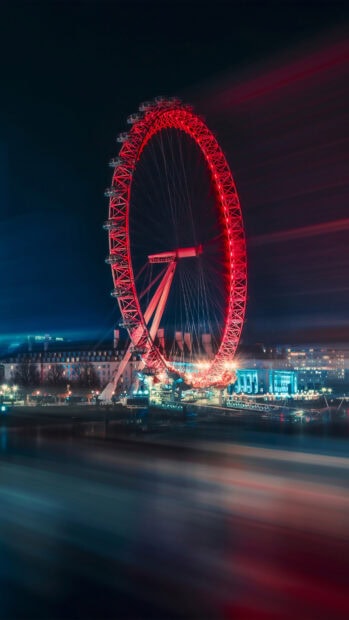 The London Eye illuminated with red lights near the river and city buildings at night, 4K Phone Wallpaper