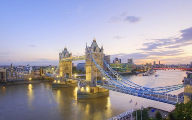 The London skyline at sunset features the illuminated Tower Bridge over the River Thames with city buildings in the background, HD Desktop Wallpaper